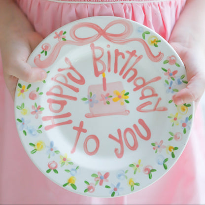 Child holding a 'Happy Birthday to you' plate with a pink dress.